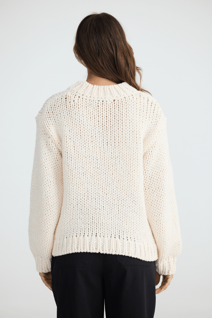 Person wearing a cream knitted sweater on a white background