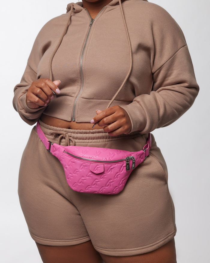 Mini monogram hot pink fanny pack with embossed logo pattern, worn around the waist over beige loungewear.