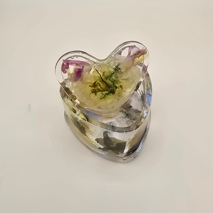 Heart-shaped resin jewelry box with embedded green and purple petals on a light background