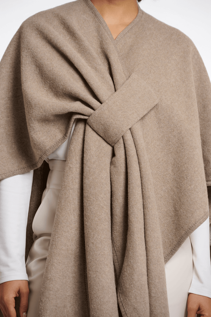 Beige poncho being worn by a person on a white background